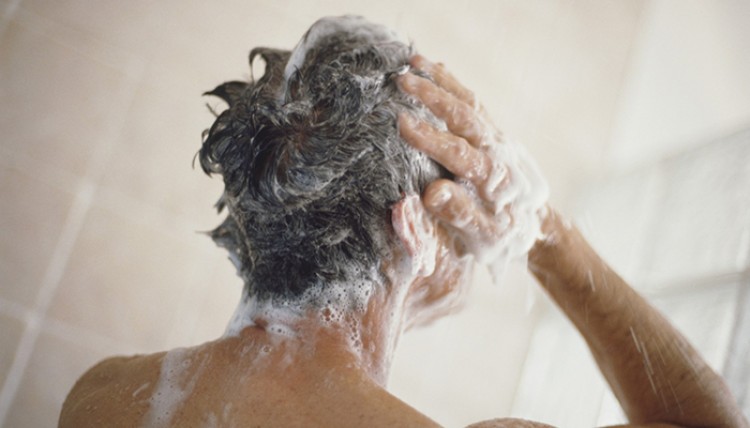 Homme prenant une douche et se lavant les cheveux, vue arrière.