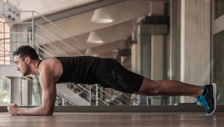 homme faisant des exercices de planche, allongé sur le ventre, les poings et les coudes au sol, sur la pointe des pieds sans toucher son ventre au sol